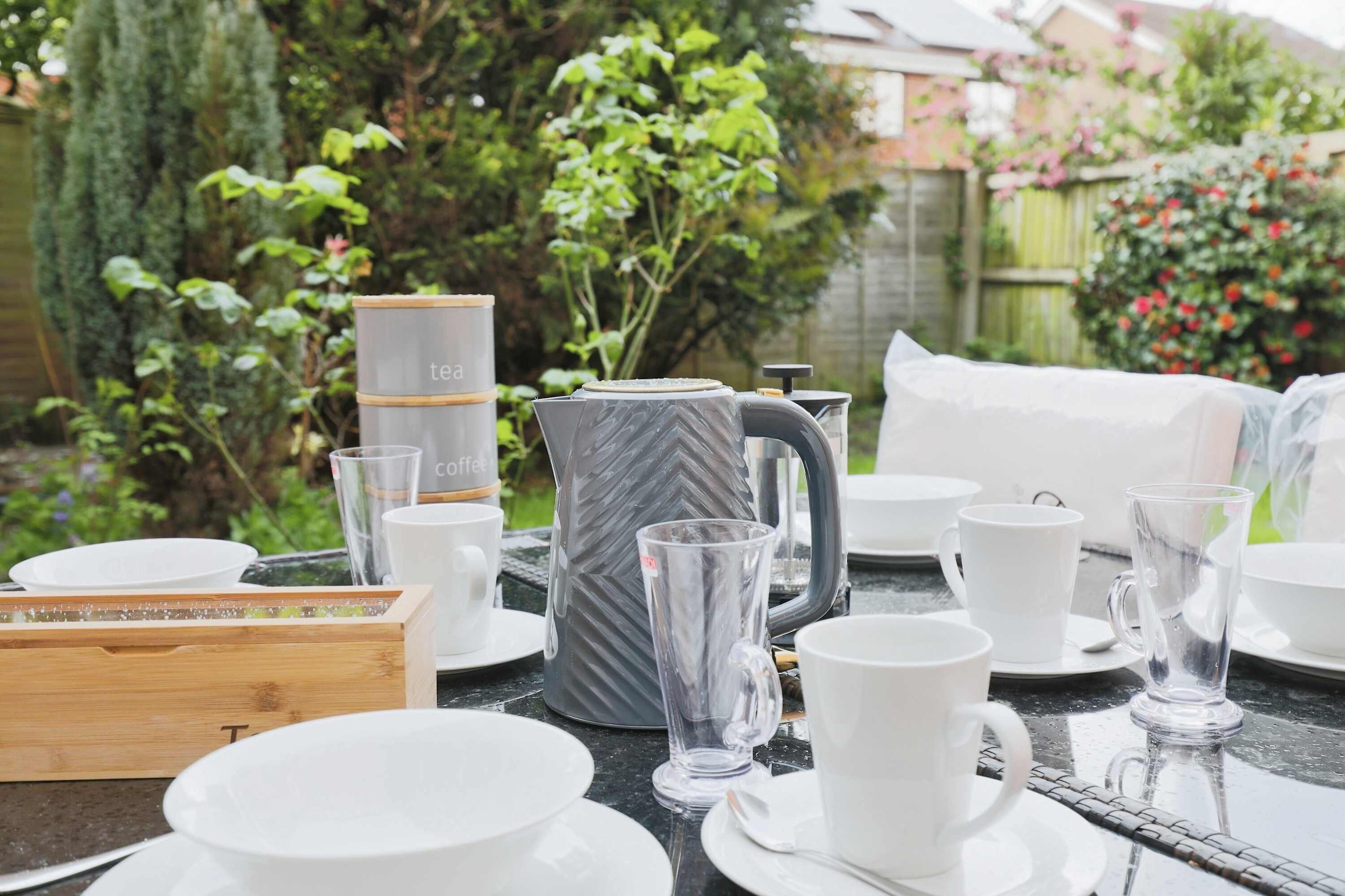 Ein Tisch im Freien mit weißen Geschirr, Gläsern und einer Kaffeemaschine.