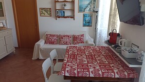 A cozy room with a sofa, a dining table, and a TV. There are framed pictures on the wall and a bookshelf with books. - Stunning Sea View Apartment in the Heart of Riomaggiore (Riomaggiore)