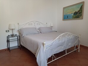 A neatly made bed with a metal frame, two bedside tables with lamps, and a painting on the wall.