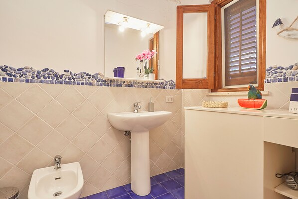 A bathroom with a pedestal sink, a bidet, and a window with blinds.