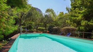 A rectangular swimming pool with a wooden deck edge, surrounded by lush greenery and trees. - Villa Majus - with swimming pool and direct access to the sea in marine protected area  (BAGHERIA)