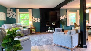 A modern living room with a grey sofa, a blue armchair, a patterned rug, and a black entertainment unit.