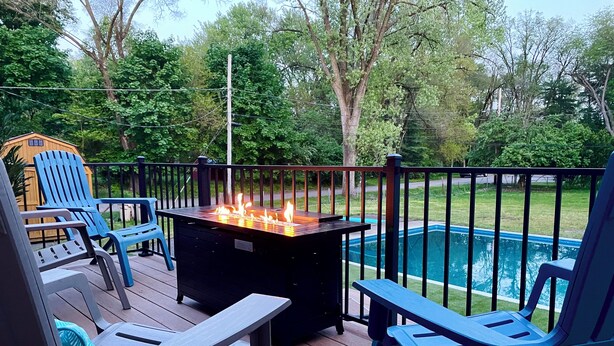 A deck with outdoor seating and a fire feature, overlooking a swimming pool.