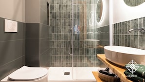 Een moderne badkamer met een douchecabine van glas, een wit toilet en een grote wastafel met een spiegel erboven.