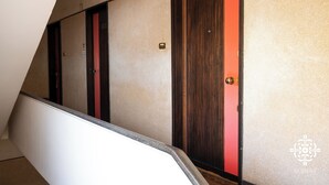 Een trap met een leuning, leidend naar een kamer met een houten deur en een rode accentmuur.