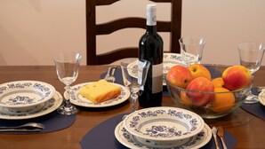 Een eettafel gedekt met borden, een fles wijn, glazen en een schaal fruit.