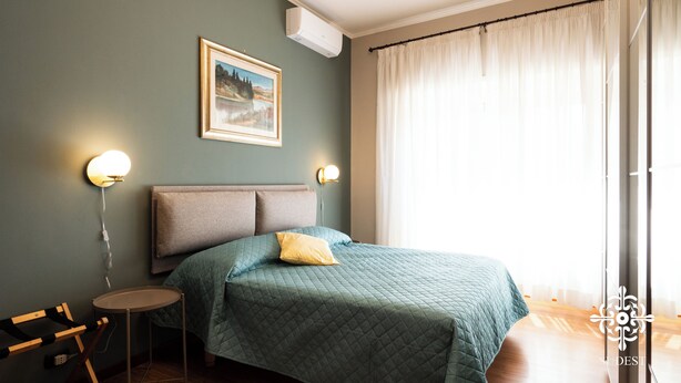 Een slaapkamer met een bed, nachtlampjes, een schilderij en een raam met gordijnen.