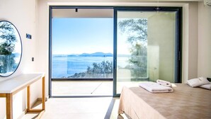Une chambre dotée d’un grand lit, offrant une vue sur la mer et donnant sur un espace extérieur grâce à une porte-fenêtre coulissante.