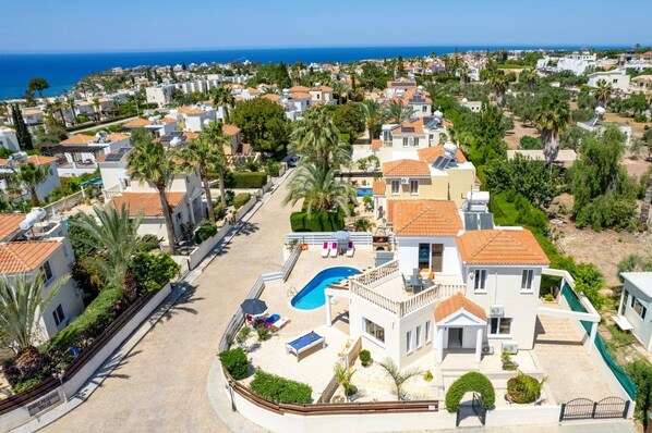 A coastal residential area with a large house featuring a swimming pool, multiple balconies, and a view of the sea.