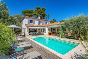 Una casa de dos pisos con piscina, mobiliario exterior y un patio cubierto.