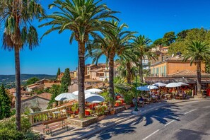 A coastal town with outdoor seating at cafes, palm trees, and buildings with red-tiled roofs.