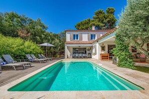 Ein zweistöckiges Haus mit Swimmingpool, Sitzgelegenheiten im Freien und einem Garten.