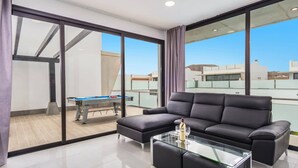 A modern living room with a glass coffee table, a black leather sofa, and a pool table.