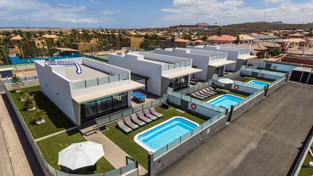 A modern hotel with multiple swimming pools, a rooftop terrace, and a view of the surrounding landscape.
