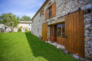 Un edificio de piedra con puerta y ventanas de madera, un césped bien cuidado y un cielo despejado.