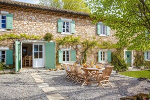 A stone house with a gravel patio and wooden furniture. - Villa Le Vieux Mas by Villa Plus (Aubussargues)