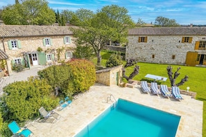 A stone building with a swimming pool, lounge chairs, and a well-maintained lawn.