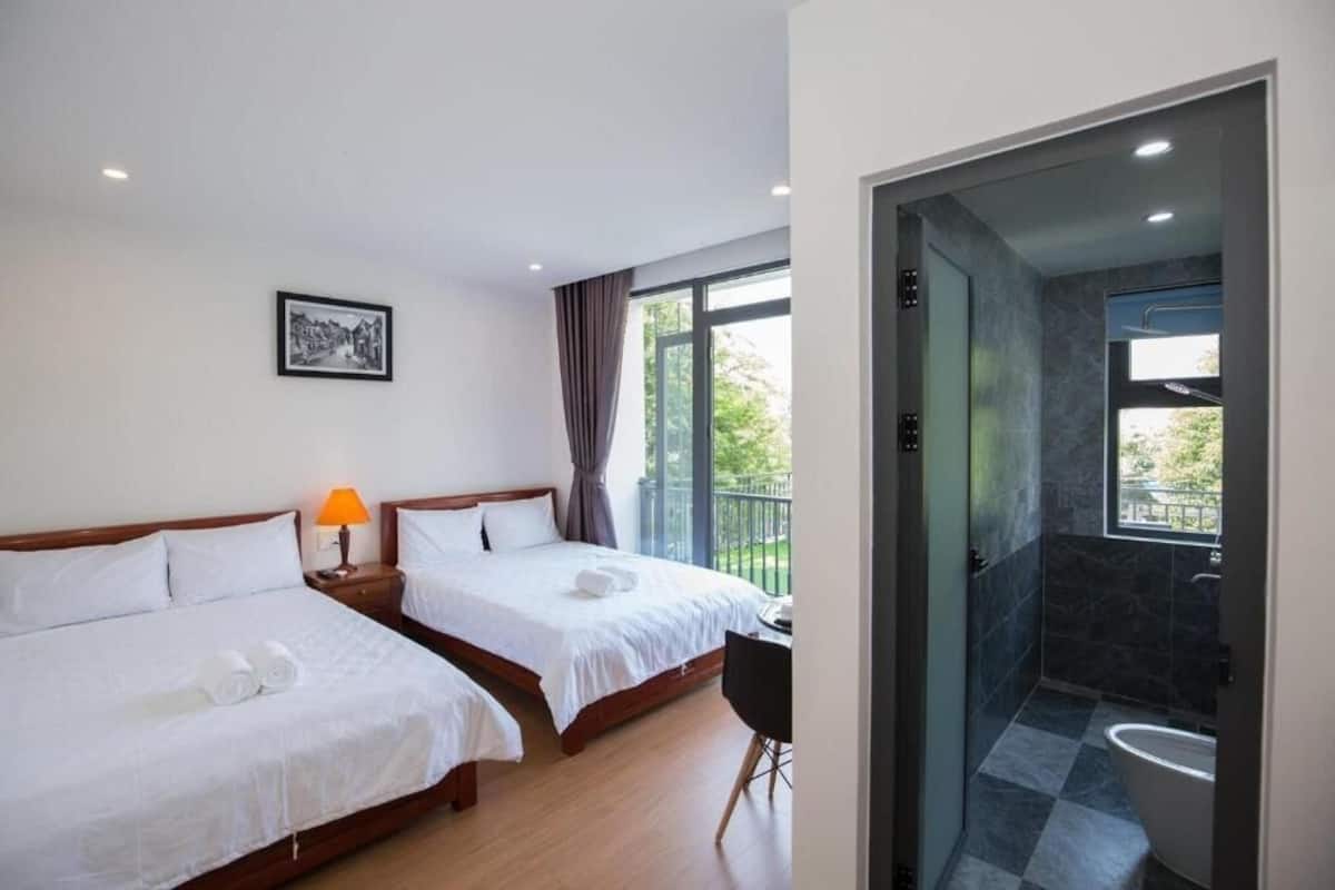 A hotel room with two beds, a desk, a chair, a balcony, and a bathroom.