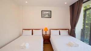 A hotel room with two beds, a nightstand with a lamp, a framed picture on the wall, and a window with curtains. - Seimy Homestay (Da Nang)