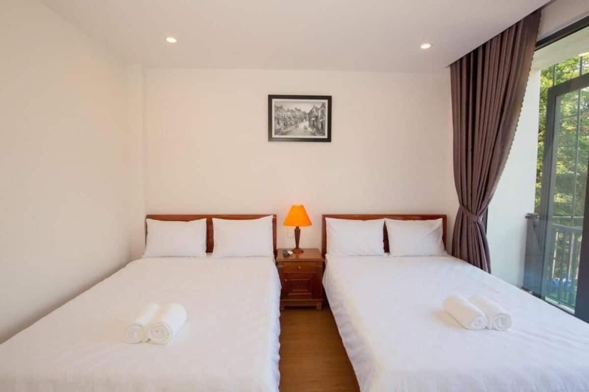 A hotel room with two beds, a nightstand with a lamp, a framed picture on the wall, and a window with curtains.