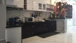 A modern kitchen with black cabinets, white countertops, and a black island. There are various appliances including a microwave, kettle, and toaster. The kitchen has a tiled backsplash and a black rug on the floor. - Seimy Homestay (Da Nang)