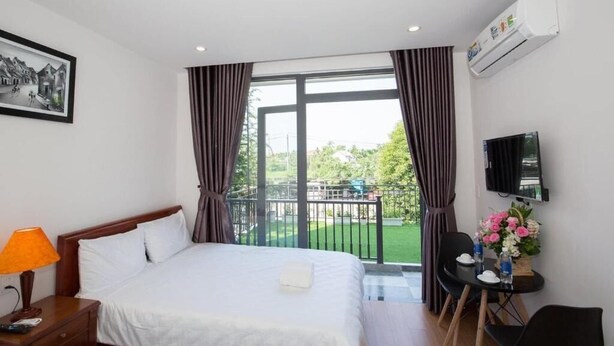 A hotel room with a bed, a desk with a chair, a TV, and a balcony with curtains. - Seimy Homestay (Da Nang)