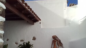 Une terrasse dallée de pierres, ornée d’une statue, d’un pot de fleurs et d’un escalier menant à un mur blanc.