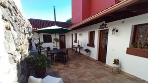 Une terrasse avec une table et des chaises, entourée de plantes en pot et d’un mur de pierre.