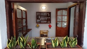 A narrow hallway with a wooden door frame, a shelf with kitchenware, and potted plants. - Finca La Sirena Vacation Apartments - Apt. # 9 Garachico (San Juan del Reparo)