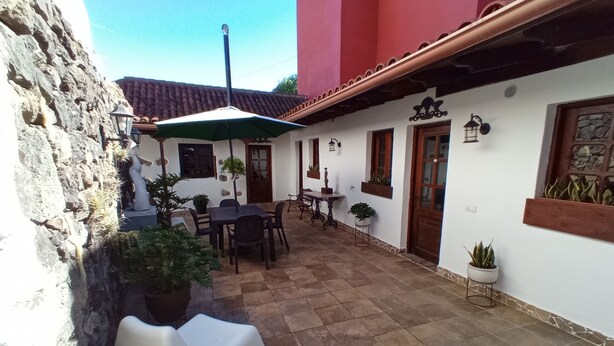 A patio with a table and chairs, surrounded by potted plants and a stone wall. - Finca La Sirena Vacation Apartments - Apt. # 9 Garachico (San Juan del Reparo)