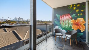 Un balcón con vistas a la ciudad, dos sillas de mimbre y un mural de flores.