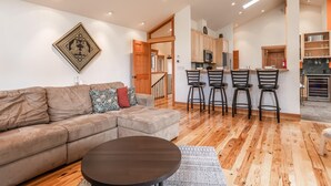 A modern living room with a sofa, a coffee table, and a kitchen area with bar stools. - Northstar Home w/Rec Center Access (Truckee)