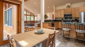 A spacious living area with a wooden dining table, a kitchen with wooden cabinets, and a large window providing natural light. - Northstar Home w/Rec Center Access (Truckee)
