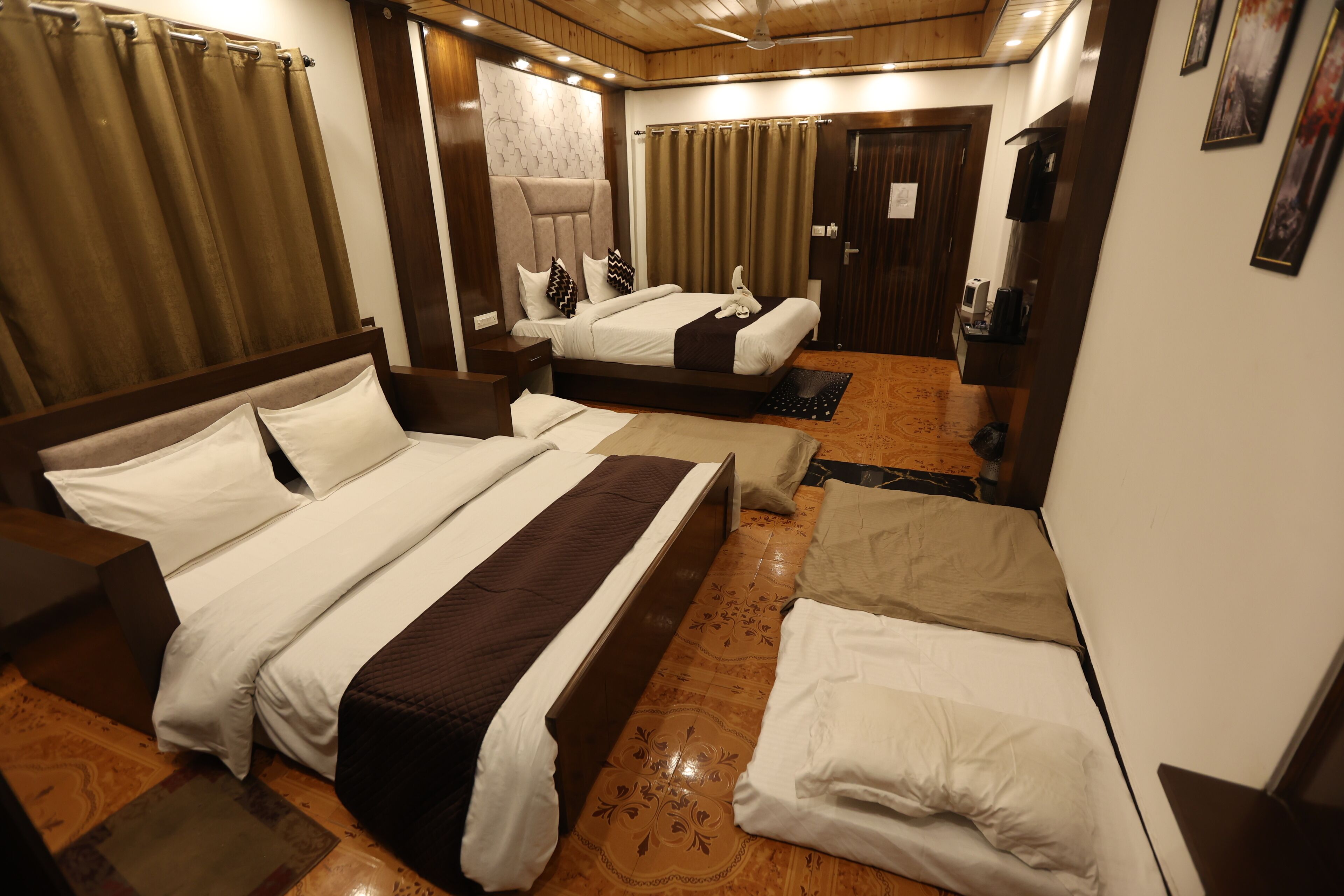 A hotel room with two beds, a wooden floor, a ceiling fan, and a small desk with a chair.