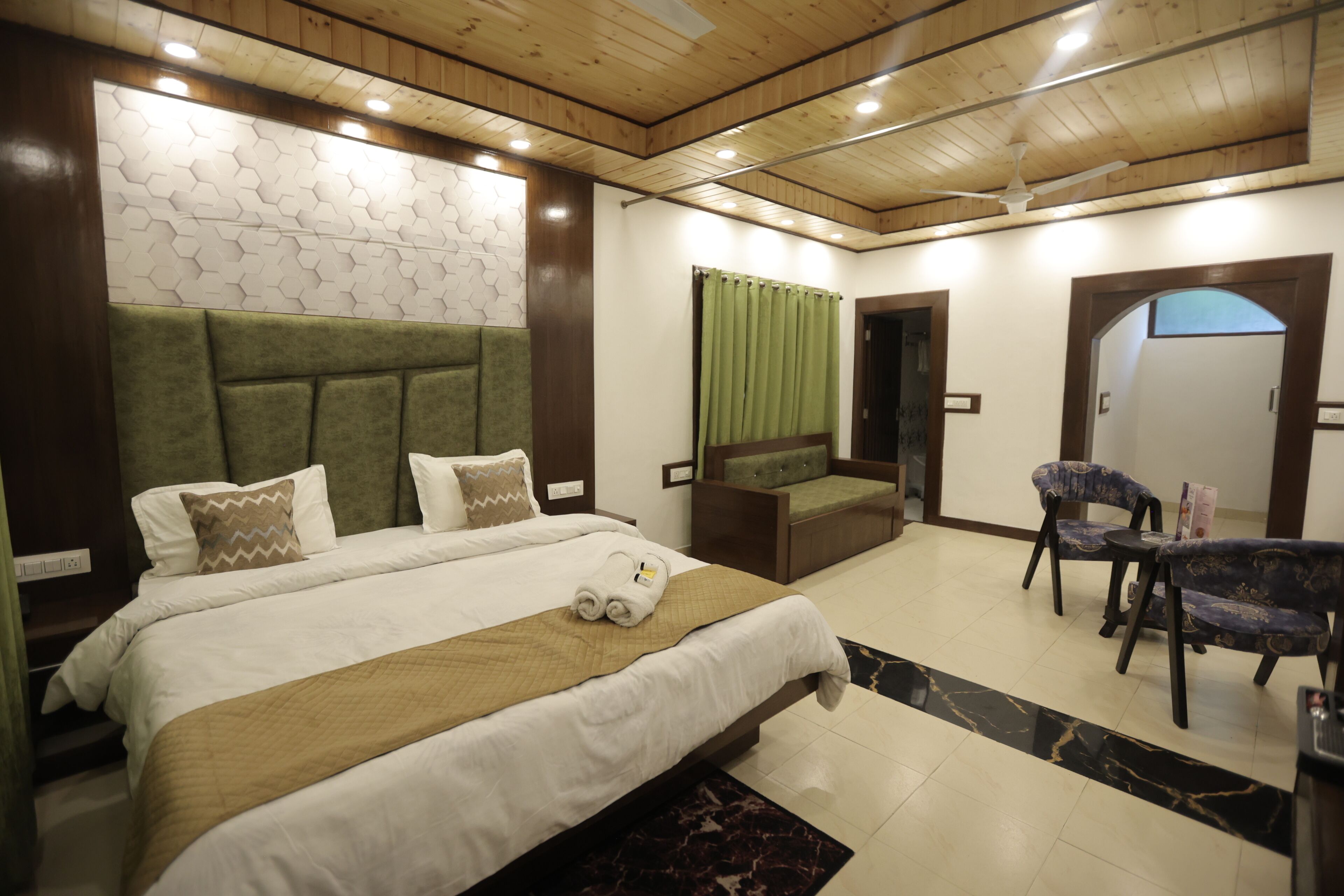 Habitación de hotel con una cama grande, un sofá, una mesa de comedor con sillas y un ventilador de techo.
