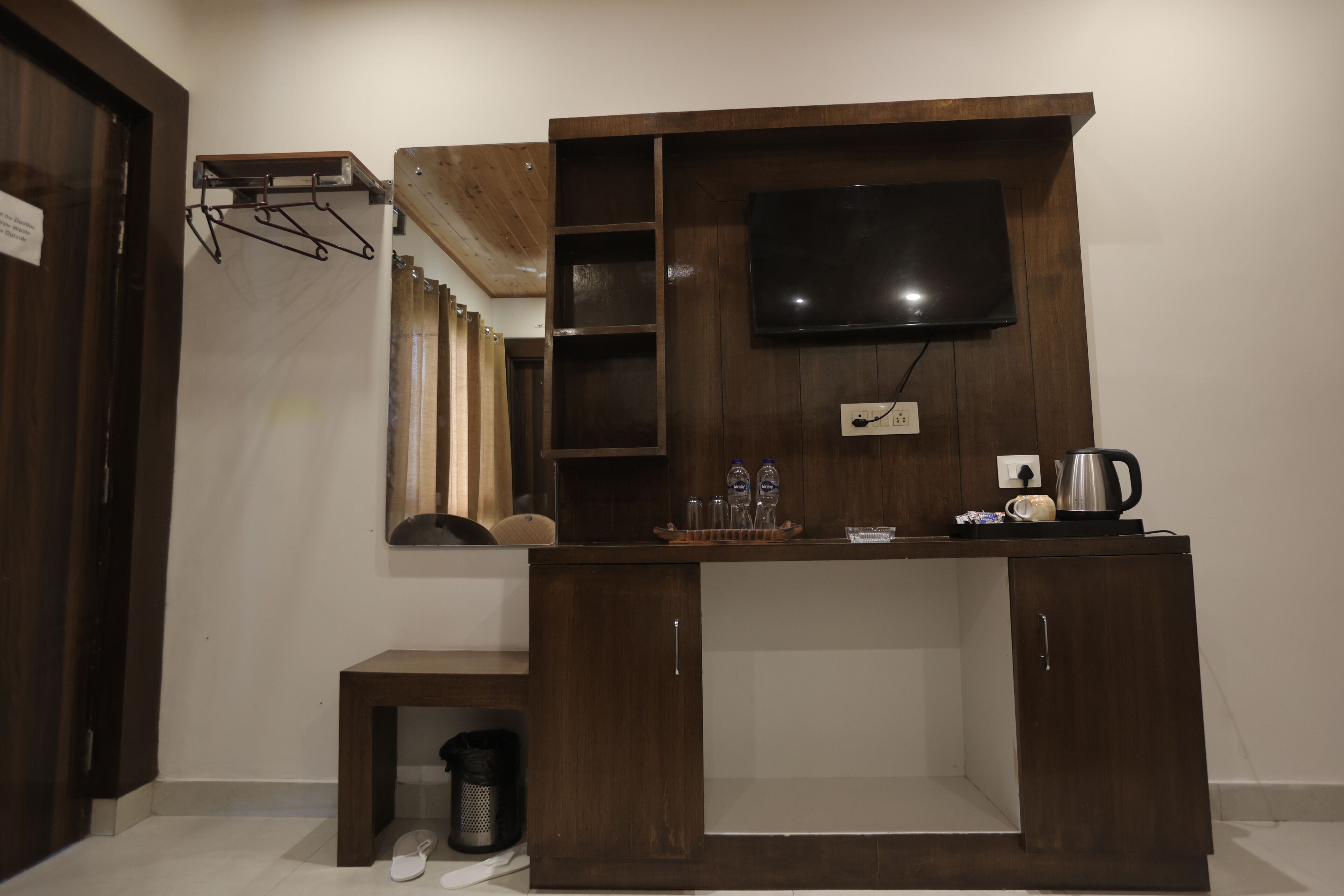Een kamer met een houten kast, een flatscreen televisie aan de muur en een tafeltje met een waterkoker en kopjes.