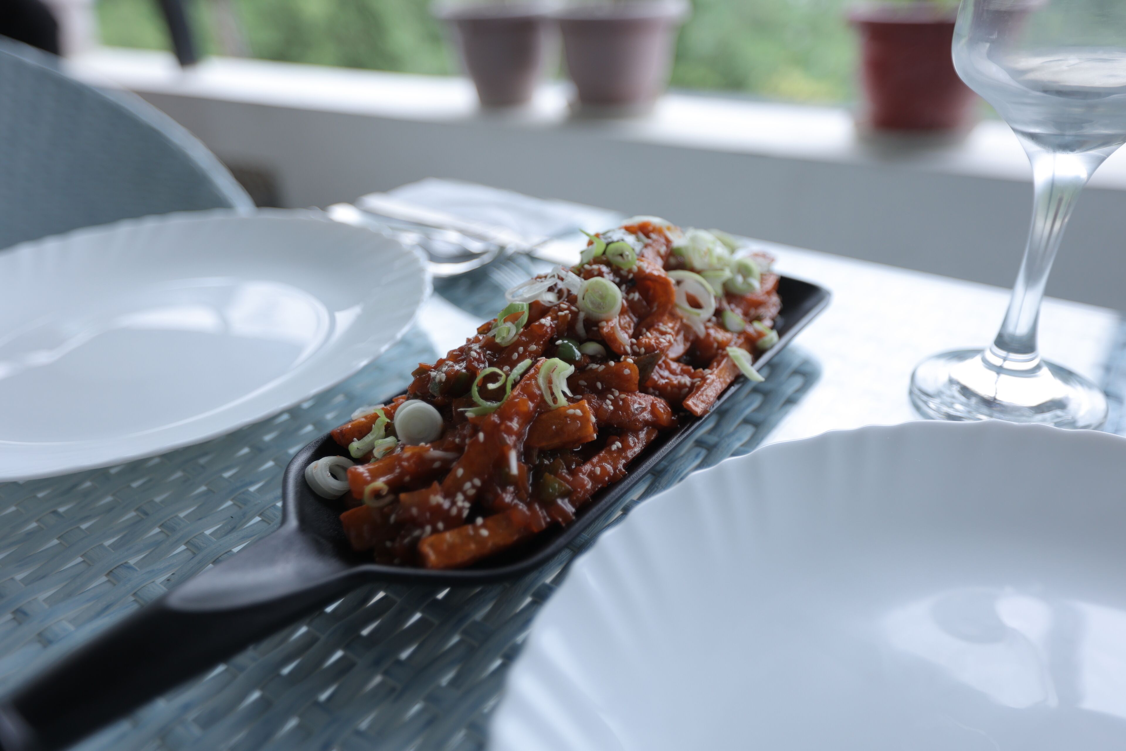 Una mesa de comedor con un recipiente rectangular de comida, una copa de vino y un plato blanco.