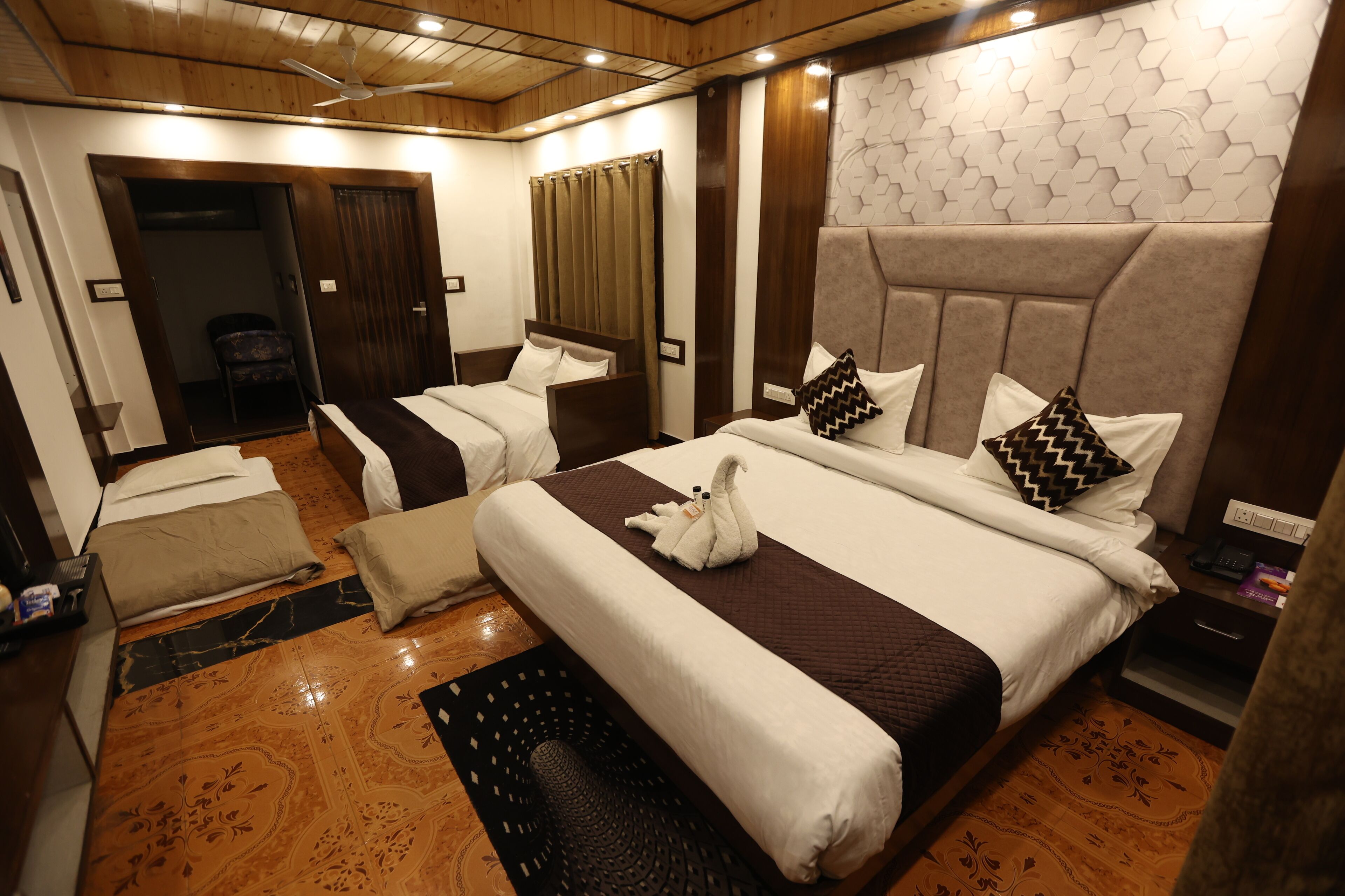 A hotel room with two beds, a sofa, a small table, and a wall with a geometric pattern.