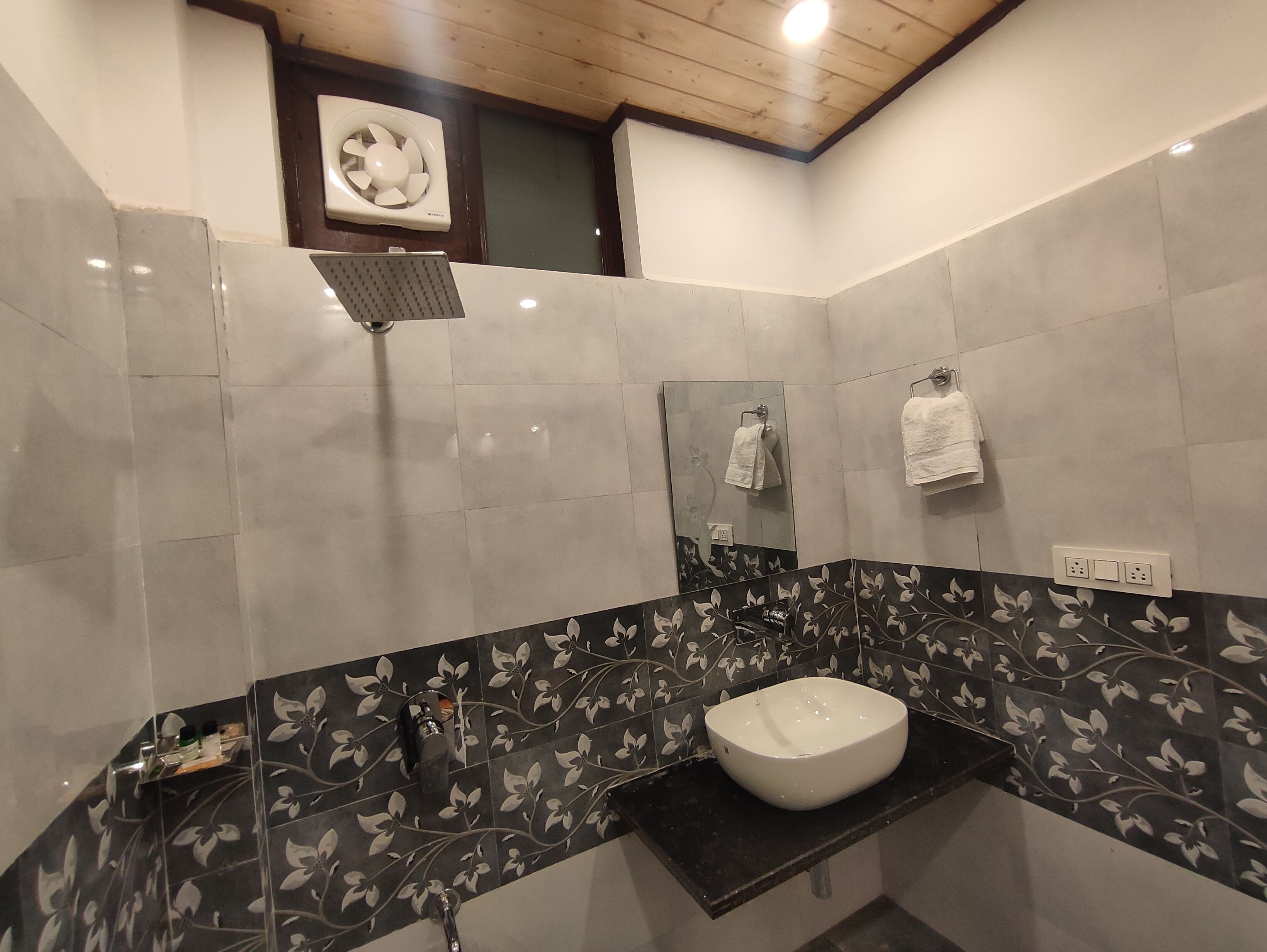 A bathroom with a white sink, black floral tiles, a mirror, and a ceiling fan.