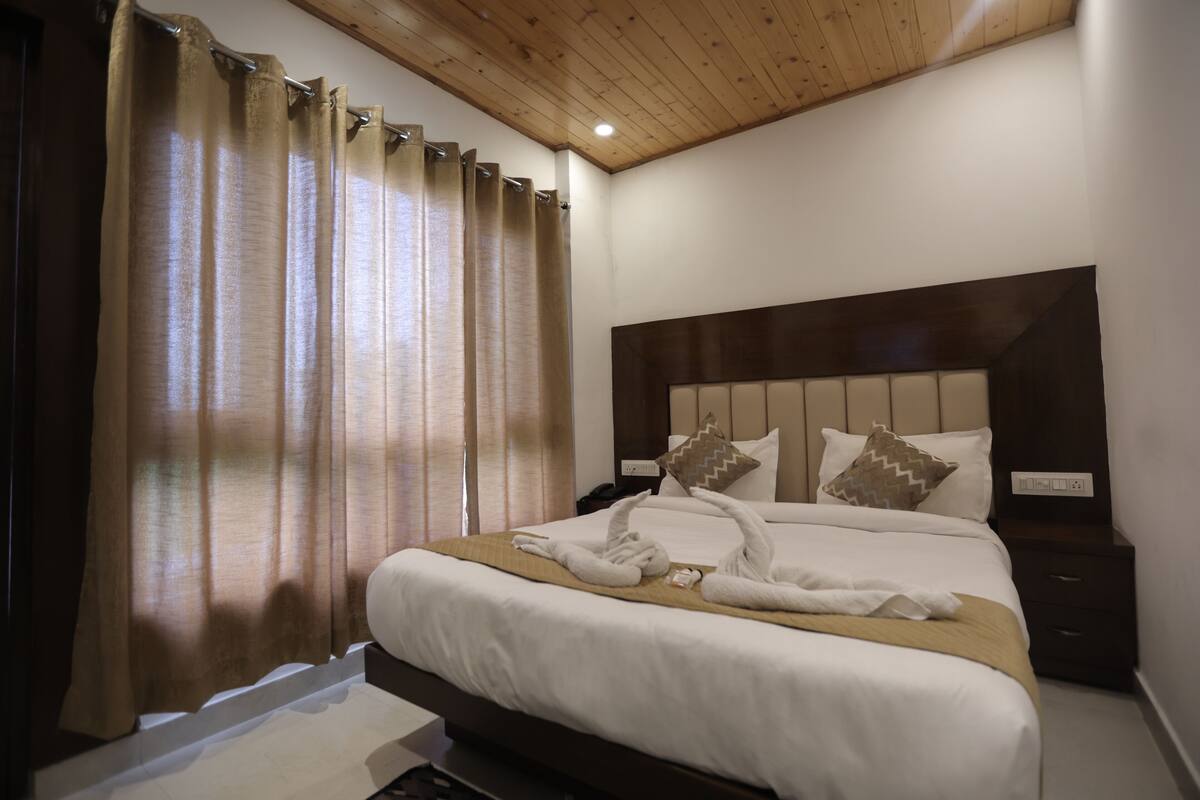 A hotel room with a wooden ceiling, a large bed with white bedding, two pillows, and a nightstand.