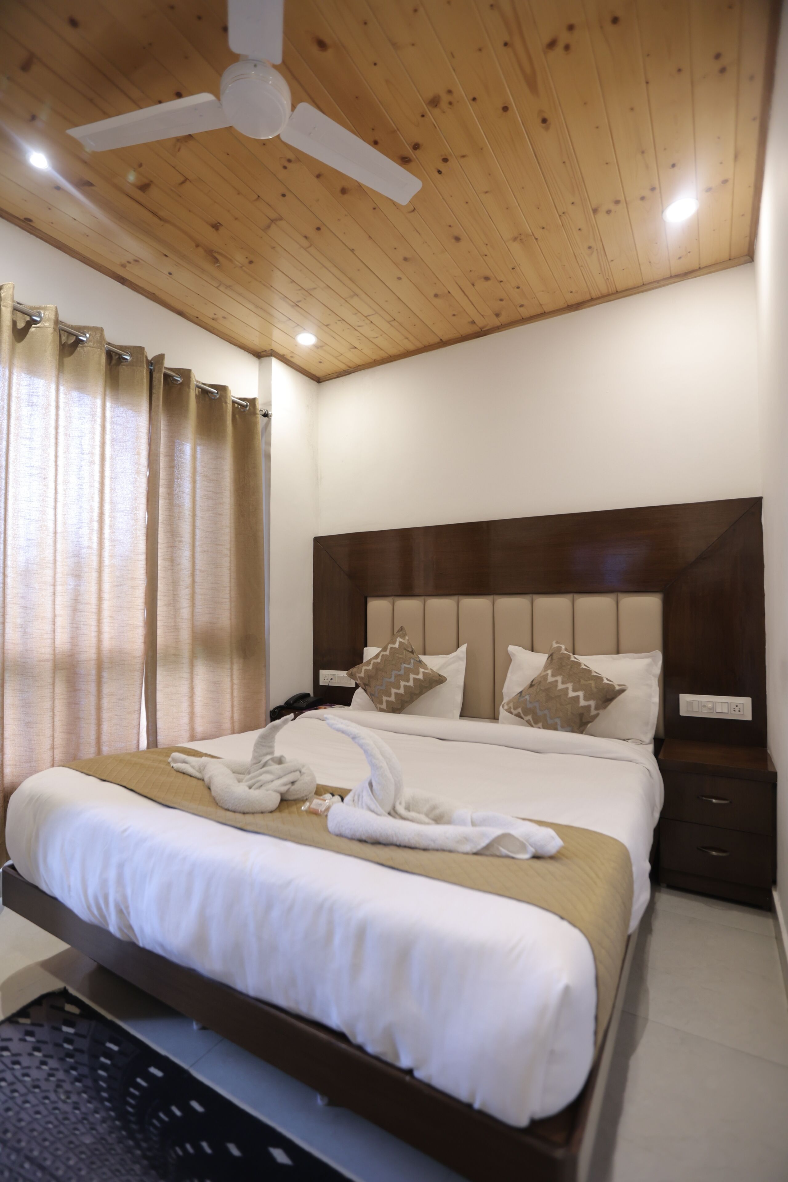 A neatly made bed with a wooden headboard, a ceiling fan, and a bedside table with a lamp.