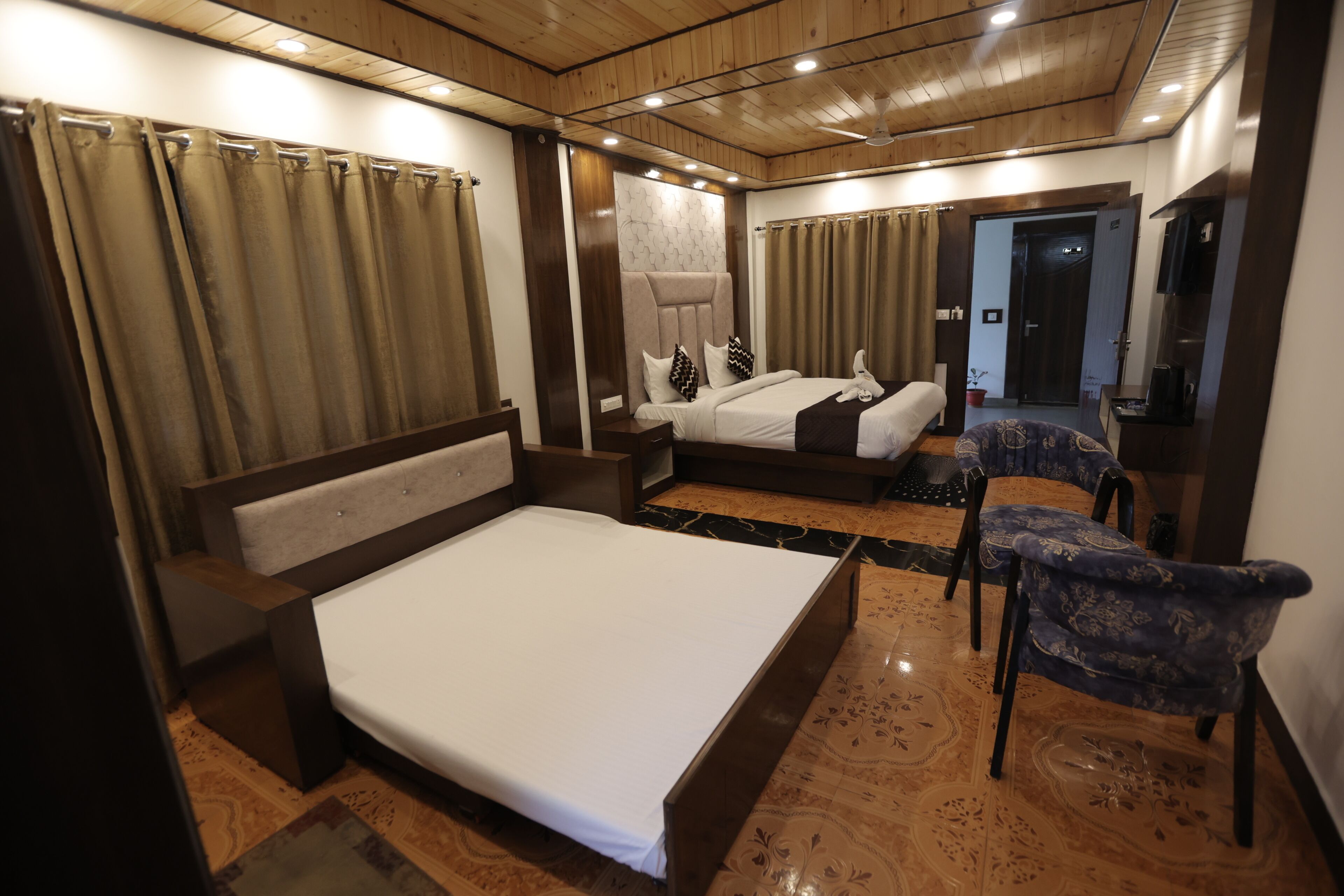 A hotel room with a large bed, a smaller bed, a seating area, and a bathroom visible through an open door.