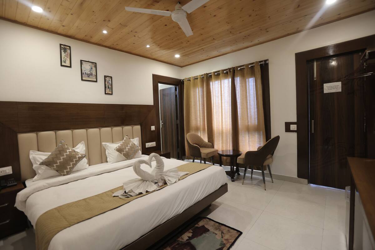 A hotel room with a large bed, a wooden ceiling, a desk with chairs, and a door.