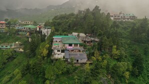 A multi-story building with a green roof, surrounded by lush greenery and hills. - StudioZ Paradise Hills Mussoorie (Mussoorie)