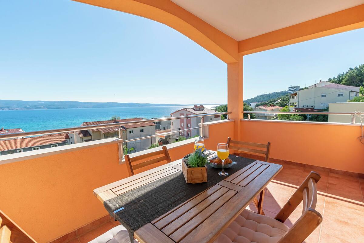 A balcony with a wooden table, chairs, and a potted plant.