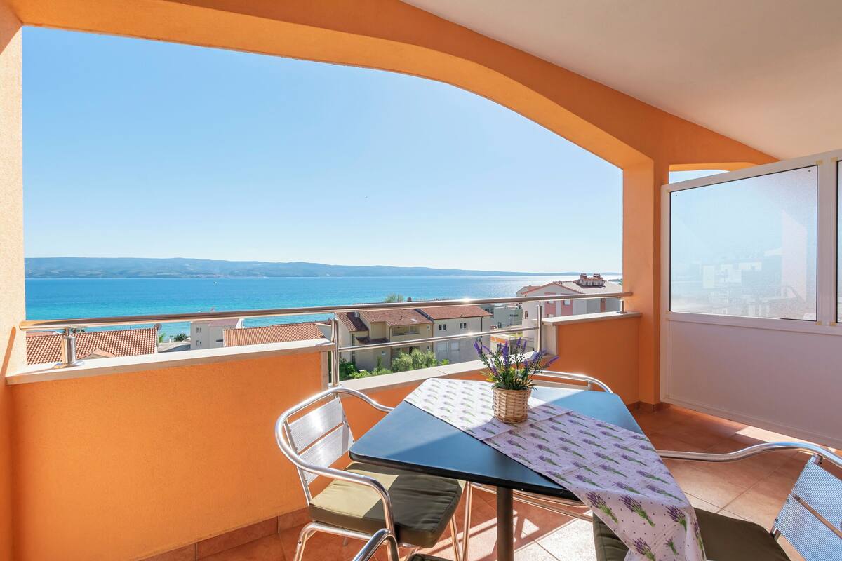 A balcony with a table and chairs, overlooking a coastal view.