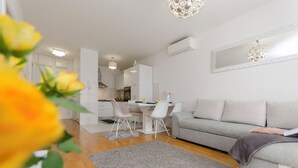 A modern living room with a grey sofa, a dining table with chairs, and a kitchen area in the background. - Apartment L and I (Sibenik)