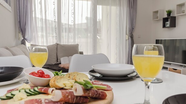 A dining table with a charcuterie board, two glasses of yellow drink, and a TV in the background. - Apartment L and I (Sibenik)