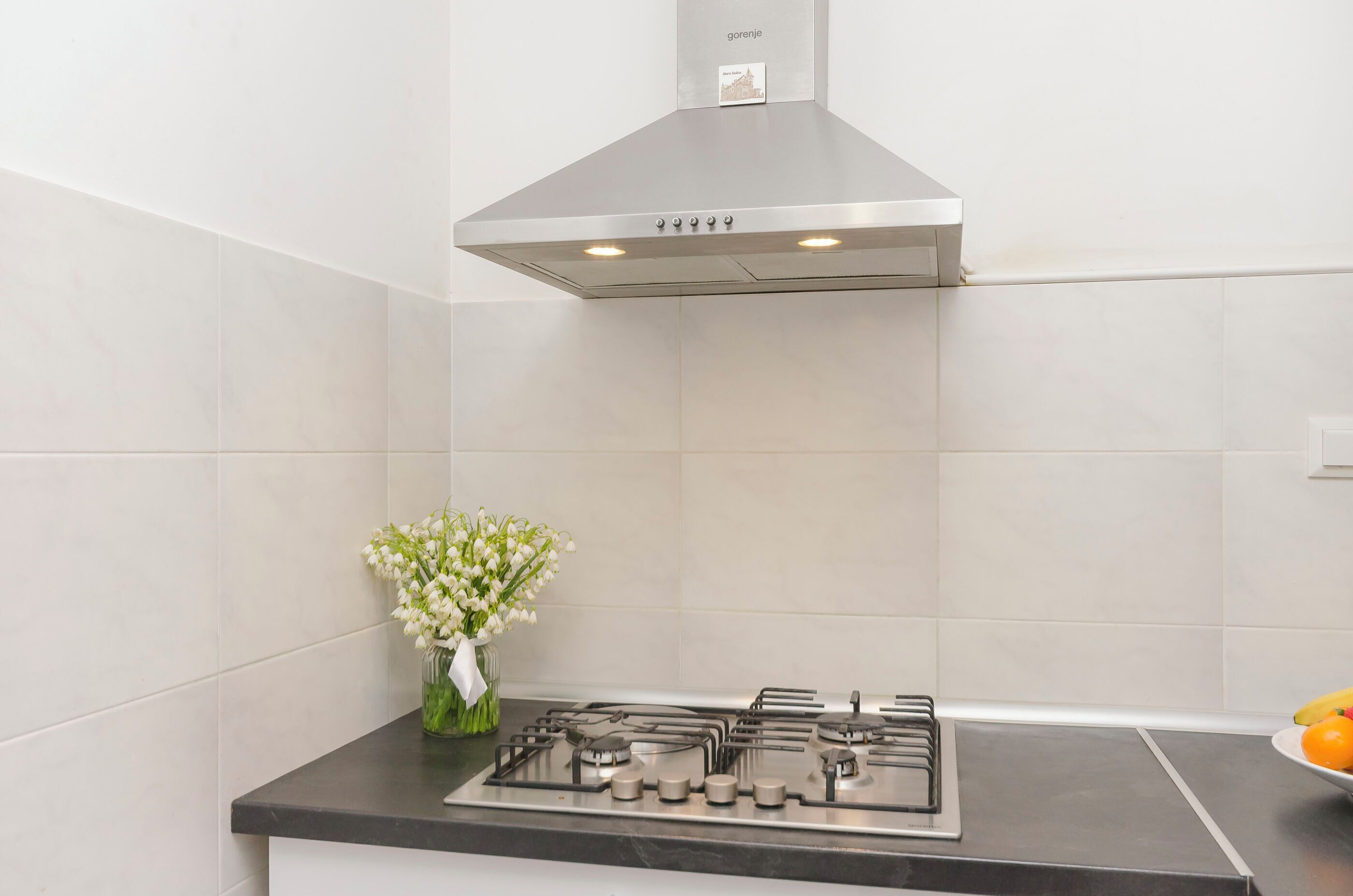 A modern kitchen with a stainless steel range hood, a gas stove, and a vase of white flowers on the counter.