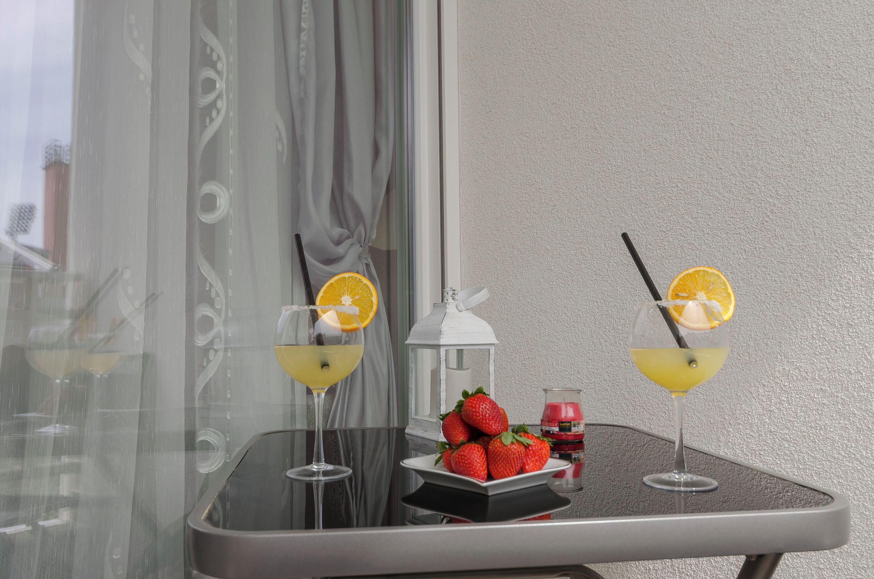 A table with two glasses of a yellow beverage, each garnished with an orange slice and a straw, and a plate of strawberries.